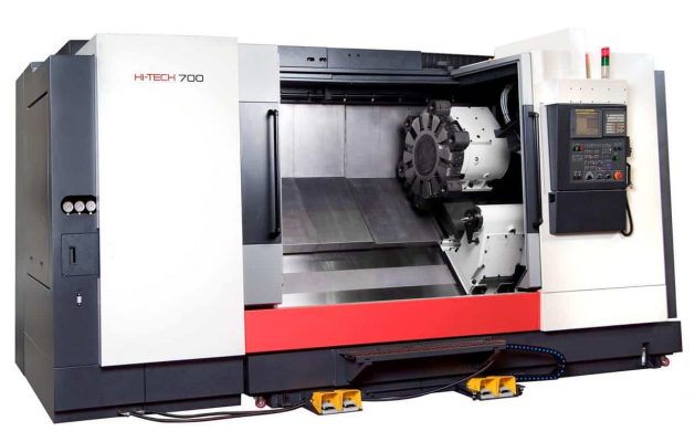 En stor CNC-maskin, märkt "H-TECH 700", med en kontrollpanel till höger och ett verktygstorn i mitten inuti maskinens hölje.