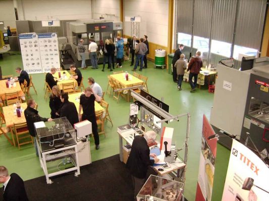 Människor deltar i en maskin- och teknikutställning i en stor inomhuslokal. De engagerar sig med olika bås, displayer och demonstrationer med industriell utrustning.