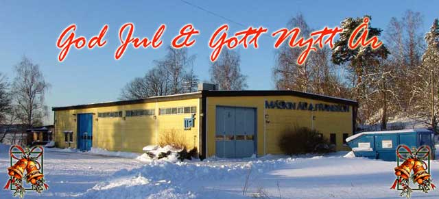 En gul byggnad med snö på marken, omgiven av träd. Texten "God Jul & Gott Nytt År" är skriven i rött överst på bilden, vilket översätts till "God Jul & Gott Nytt År.