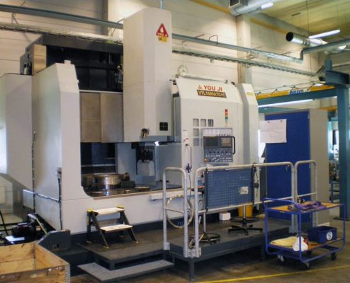 En stor industriell CNC-maskin i fabriksmiljö, omgiven av säkerhetsräcken och i anslutning till en vagn med olika verktyg.