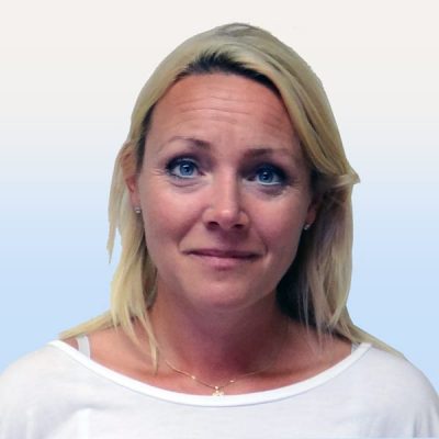 Porträtt av en kvinna med blont hår, klädd i en vit topp, mot en enkel bakgrund, med ett lätt leende.