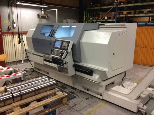En cnc-svarvmaskin i industriell miljö, omgiven av metallstänger och annan tillverkningsutrustning.
