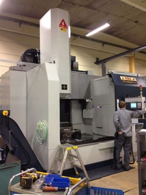 En tekniker driver en stor industriell cnc-maskin i en verkstad, omgiven av olika verktyg och utrustning.