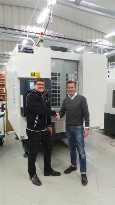 Två män skakar hand framför en stor industrimaskin inne i en fabrik.
