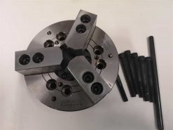 Närbild av en metallsvarvchuck med tre käftar och flera svarta bultar, designad för att säkert hålla arbetsstycken under bearbetning. Basen är graverad med "Licensed by Kitagawa.